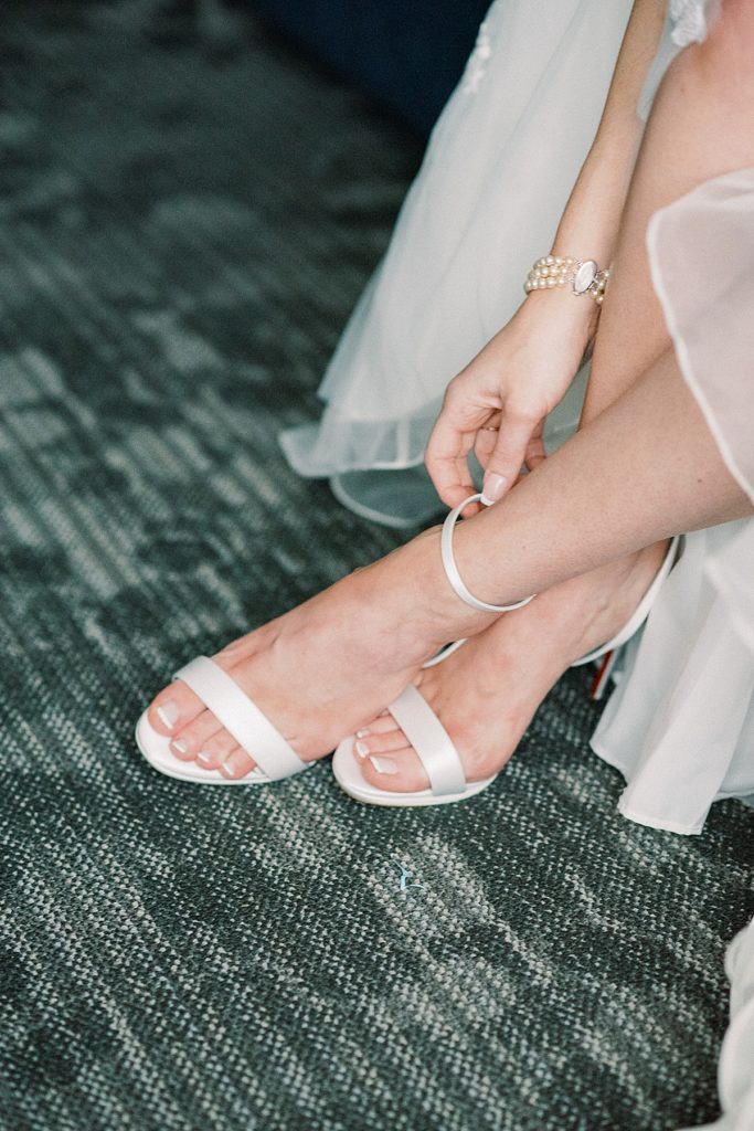 Classic portrait of the bride as she buckles her Christian Louboutin couture shoes by wedding photographer Michelle Behre Photography..